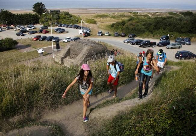 Youths hike up a hill past an old German bunker overlooking the former D-Day landing zone of Omaha Beach near Colleville sur Mer