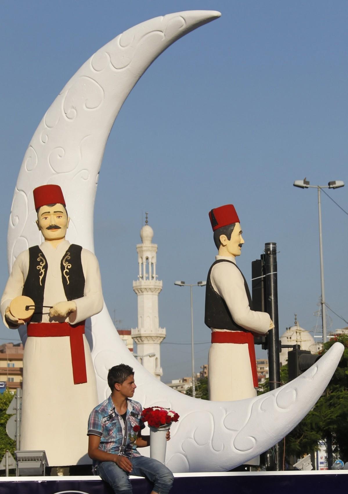 A vendor sits near statues of Musaharati, or dawn awakeners, erected as part of decorations ahead of the holy fasting month of Ramadan at the port city of Sidon Ramadan 2014