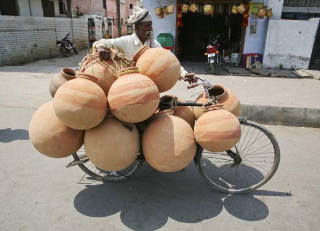 A potter transports earthen pots on his bicycle to sell in a market on a hot day. These pots are mainly used in summers to keep drinking water cold. Overloaded India