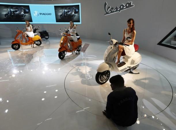 Models sit on scooters at the Vespa pavilion as a worker cleans the floor during the Indian Auto Expo in Greater Noida.