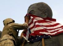 A U.S. Marine covers the face of a statue of Iraqi President Saddam Hussein with a U.S. flag in Baghdad, on April 9, 2003. U.S. troops briefly draped an American flag over the face of a giant statue of Hussein, as they prepared to topple it in front of a