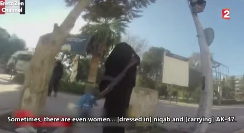 A woman in Niqab armed with AK 47 carries a child into a park.