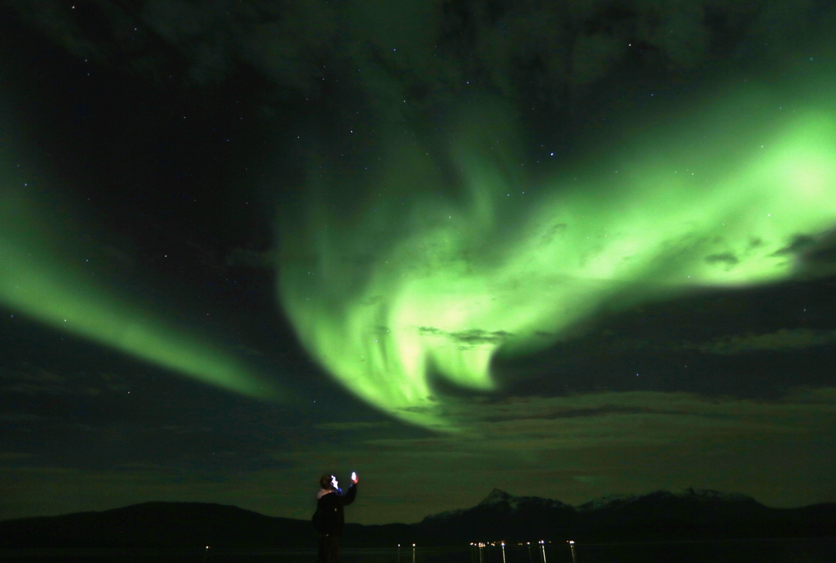 A tourist takes photos of Aurora Borealis (Northern Lights) over the Bals-Fiord north of the Arctic Circle, near the village of Mestervik. Aurora Borealis (Northern Lights) over the Bals-Fiord north of the Arctic Circle