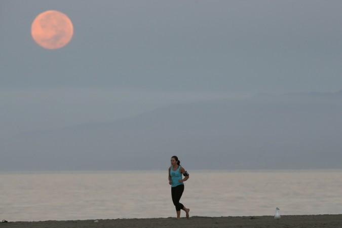 A woman jogs on a beach with the moon in the background in Santa Monica, California Blood Moon