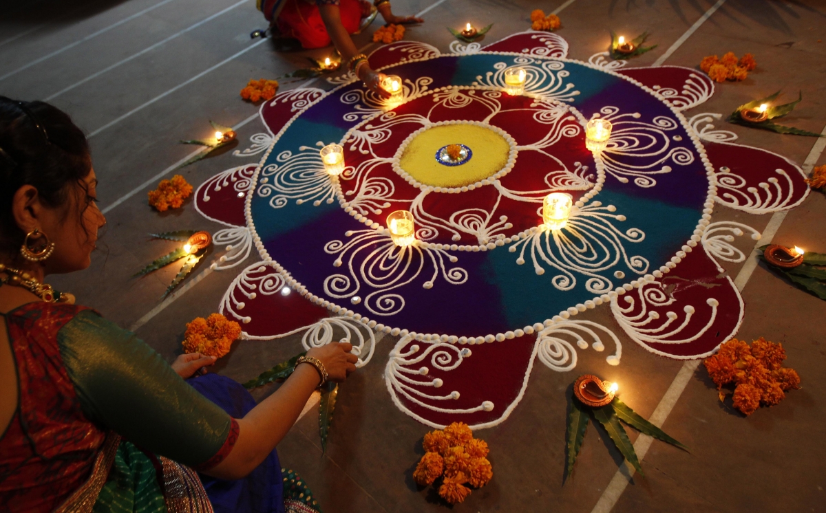 Hindu women arrange oil lamps and flowers around a Diwali 2014