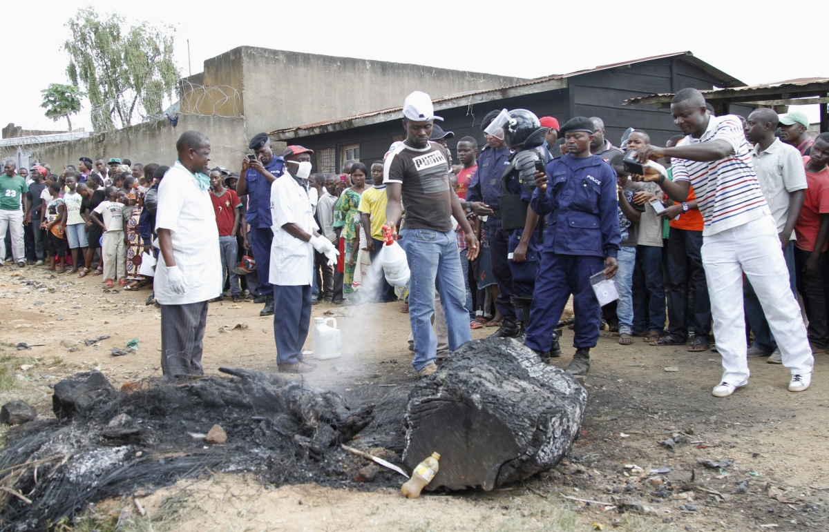 A man extinguishes the burnt remains of a man who was lynched by a mob, as policemen take photographs, in Beni, in the Democratic Republic of Congo's North Kivu province, October 31, 2014.