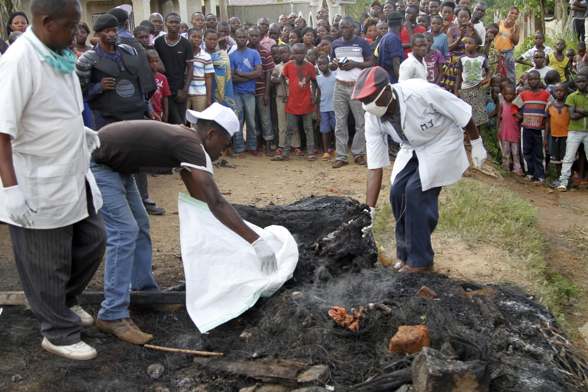 A man extinguishes the burnt remains of a man who was lynched by a mob, as policemen take photographs, in Beni, in the Democratic Republic of Congo's North Kivu province, October 31, 2014.