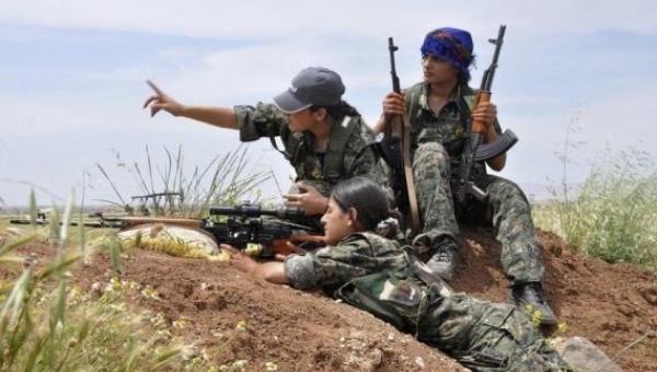 A Kurdish Woman's Protection Unit,YPJ sniper takes position on a hill,while her colleagues watch on.