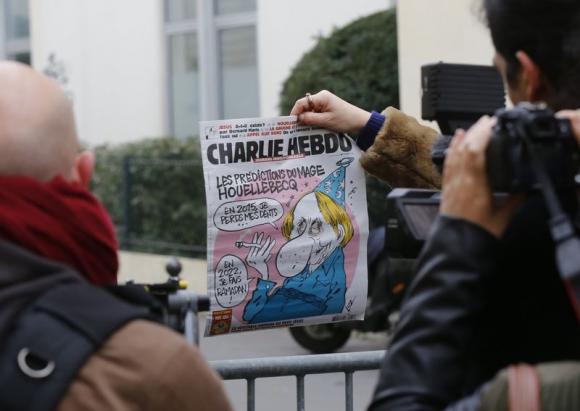 A member of the media makes images of the front page of Charlie Hebdo which shows a caricature of French author Michel Houellebecq near the Paris offices of Charlie Hebdo, a satirical newspaper, after a shooting January 7, 2015. Charlie Hebdo
