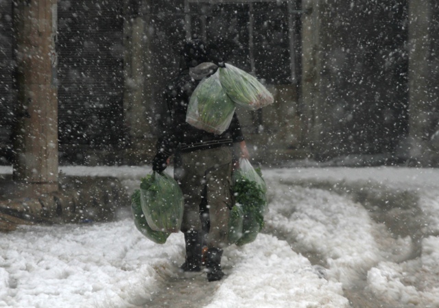 A man carries bags of vegetables as he makes his way through snow in the Duma neighbourhood of Damascus. Syria Snow