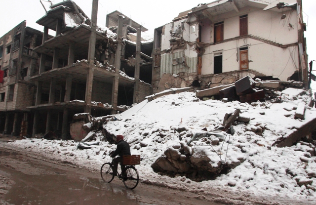 A man rides a bicycle past damaged buildings covered with snow in the Duma neighbourhood of Damascus. Syria Snow