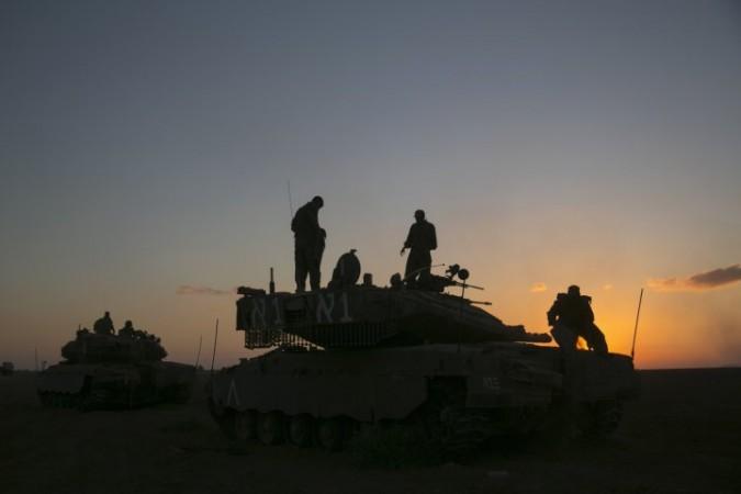 Israeli soldiers stand on top of a tank near Gaza