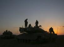 Israeli soldiers stand on top of a tank near Gaza