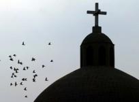 A flock of birds flies past a cross atop a Christian church in Baghdad