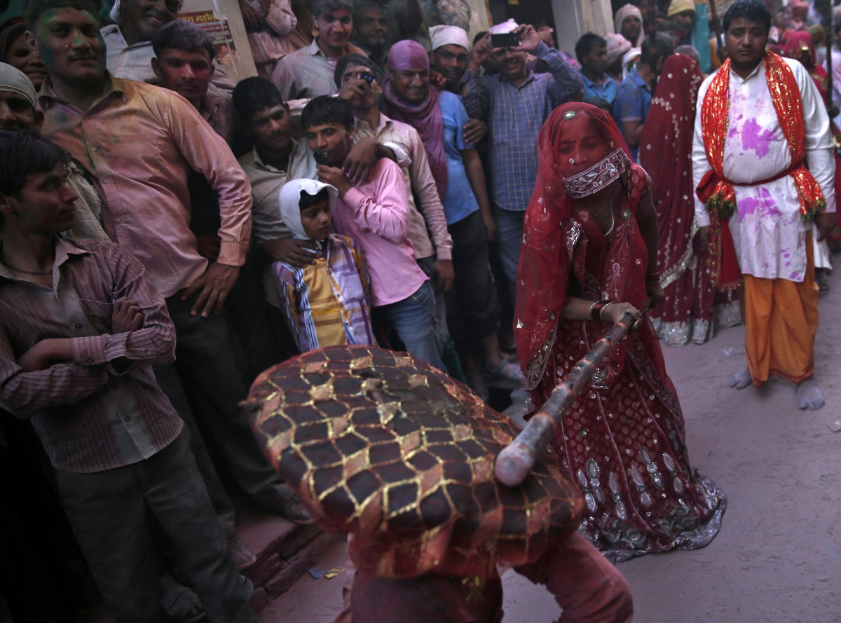 A man shields himself from a woman playfully beating him with a stick during Holi 2015: Spectacular Images of 'Lathmar Holi' Celebrated in Mathura, Vrindavan