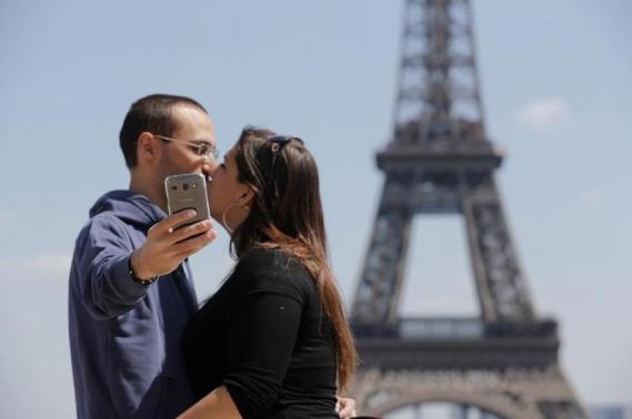 A couple of tourists use a mobile phone to take a selfie picture as they kiss at the Trocadero Square near the Eiffel Tower in Paris, May 16, 2014.