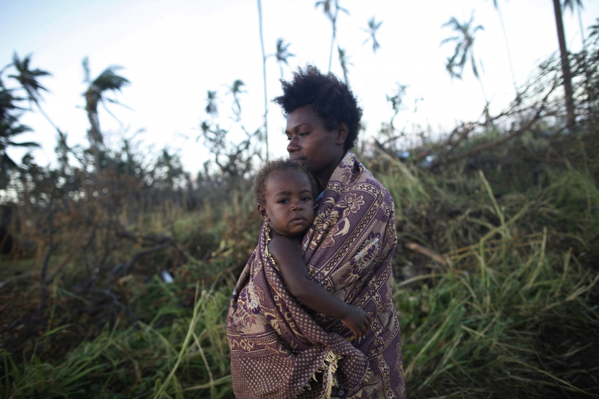 A woman carrying her baby walks past fallen trees in Tanna March 18, 2015. Vanuatu cyclone Pam
