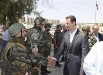 Syria's President Bashar al-Assad (R) shakes hands with a member of a military personnel.