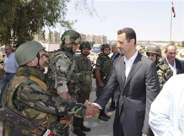 Syria's President Bashar al-Assad (R) shakes hands with a member of a military personnel.