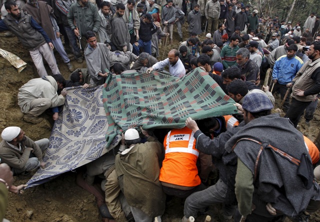 Villagers and rescue workers use blankets to cover the bodies of victims amongst the rubble after a hillside collapsed onto a house at Laden village, west of Srinagar. Kashmir Floods