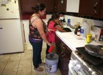 Marisela Corona, 26, (L) whose well has run dry, washes dishes with her daughter Andrea Andrade Corona, 8, from a water bucket in Porterville, California October 14, 2014.