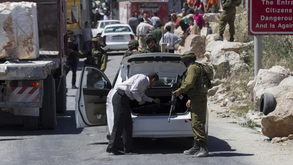 An Israeli soldier searches a Palestinian vehicle at a checkpoint near Hebron