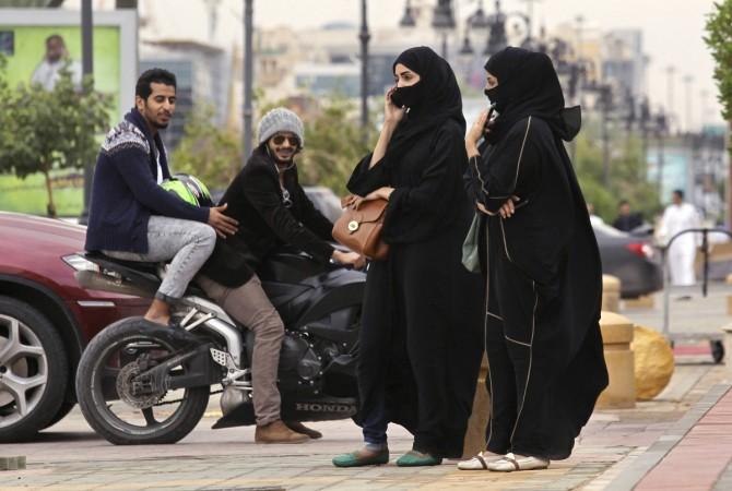 A woman speaks on the phone as men ride a motorcycle on a cloudy day in Riyadh november 17, 2013.