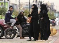 A woman speaks on the phone as men ride a motorcycle on a cloudy day in Riyadh november 17, 2013.