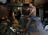 A worker operates a drilling machine as he makes parts for diesel water pumps inside his workshop in Ahmedabad, India, May 4, 2015.