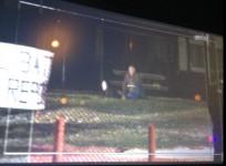 A camera footage shows a man in black hood lying on the ground, while a middle-aged man strapped with explosives sitting cross legged.