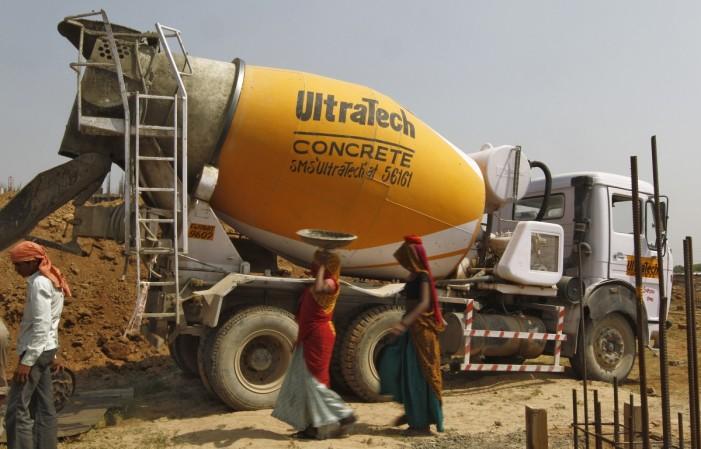 Workers walk in front of an UltraTech concrete mixture truck at the construction site of a commercial complex on the outskirts of the western Indian city of Ahmedabad April 22, 2013. ultratech cement share price, acc ambuja cements merger, lafargeholcim, cement companies in india