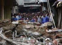 People looking on at the rubble of a collapsed building.
