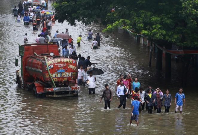 People walk through a flooded road as a water tanker is seen stuck due to heavy rains in Mumbai, India, June 19, 2015