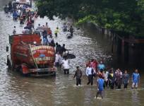 People walk through a flooded road as a water tanker is seen stuck due to heavy rains in Mumbai, India, June 19, 2015