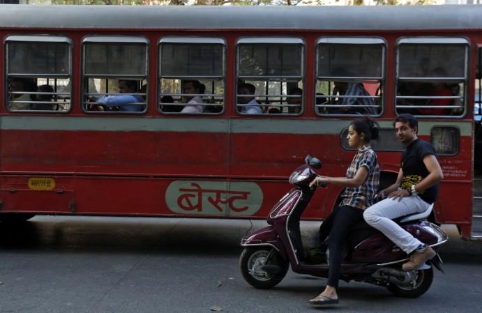 Ashok Leyland manufactures buses and trucks. A woman rides a scooter past a passenger bus on a street in Mumbai February 5, 2014 (representational image). ashok leyland sales commercial vehicles september buses share price fall demand weak row in a domestic tata motors