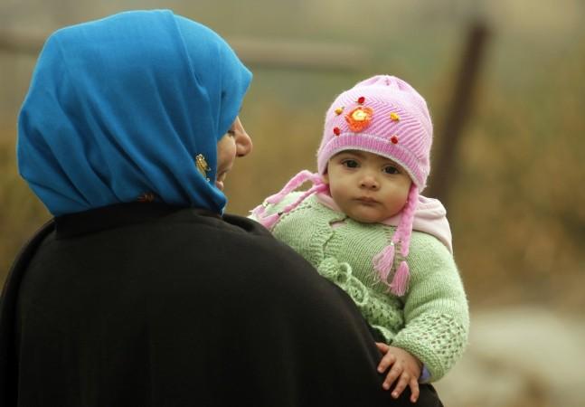 A woman walks while carrying her eight-month-old baby girl on a cold morning in Srinagar December 19, 2011 (representational image). India's $2.2 billion woolen apparel market is dominated by unorganised players, according to IDBI Capital Markets & Securities. monte carlo winter wear fashions sweaters india delhi cold temperatures stock price share bse nse gainers clothes market apparel fashions garments shawls