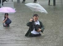 People hold umbrellas as they walk past a flooded street in Taiyuan, Shanxi Province
