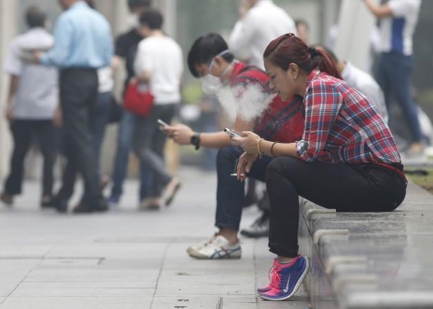 A woman smokes a cigarette next to man wearing a mask during lunch hour at the central business district in Singapore September 29, 2015 (representational image). cigarette smoking, tobacco smoking cancer, cigarette related diseases, WHO on cancer, WHO on cigarettes