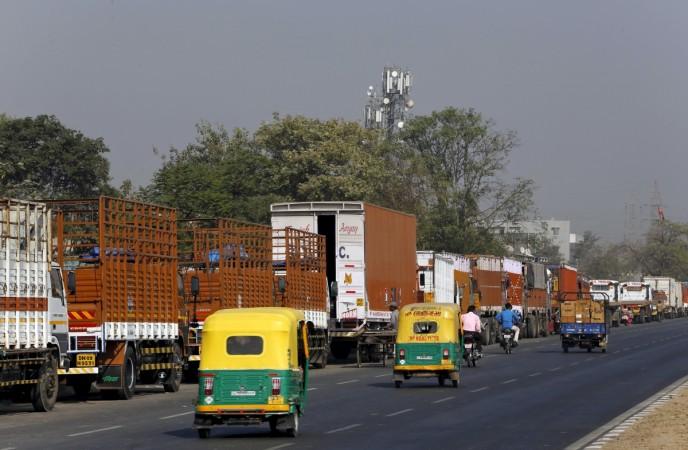 Auto rickshaws move past parked trucks along a national highway on the outskirts of Ahmedabad, India, December 2, 2015. ashok leyland, commercial vehicle sales in feb 2017, cv sales in feb 2017, ashok leyland share price, tata motors cv sales, eicher motors cv sales