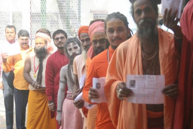 Ascetics show their voter ID cards as they wait in a queue to cast their vote at a polling booth during the 7th phase of Uttar Pradesh Assembly polls in Varanasi on March 8, 2017. uttar pradesh elections 2017, uttar pradesh exit polls, uttar pradesh election results 2017, bjp, sp, congress, pm modi, akhilesh yadav, rahul gandhi