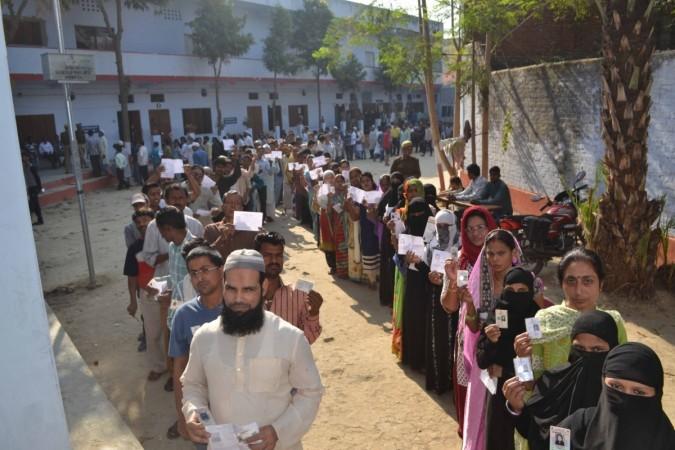 Voters show their voter ID cards as they wait in a queue to cast their vote at a polling booth during the 7th phase of Uttar Pradesh Assembly polls in Varanasi on March 8, 2017. exit polls 2017, uttar pradesh exit polls 2017, punjab exit polls 2017, goa exit polls 2017, assembly elections 2017, manipur exit polls 2017, pm modi, bjp, congress, samajwadi party