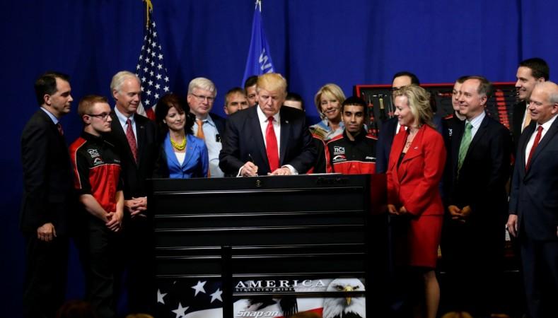 U.S. President Donald Trump signs an executive order directing federal agencies to recommend changes to a temporary visa program used to bring foreign workers to the United States to fill high-skilled jobs during a visit to the world headquarters of Snap-On Inc, a tool manufacturer in Kenosha, Wisconsin, U.S., April 18, 2017. donald trump, visa, h-1 b visa, indian students, us immigration policies, indian students in us, indian it companies