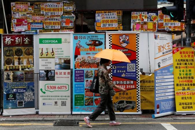 A woman walks past banners promoting retail goods and services displayed in front of closed shops for rent at the shopping Mongkok District in Hong Kong, China August 29, 2016. china, china retail sales