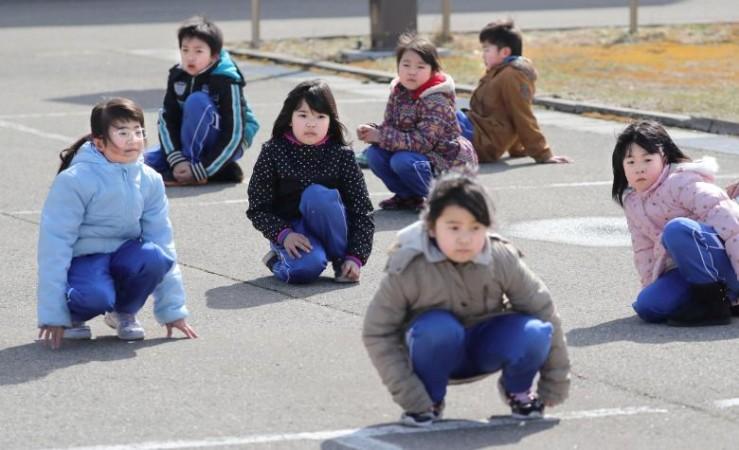 Elementary school students squat down on the street as they participate in an evacuation drill in Japan Japan evacuation dril