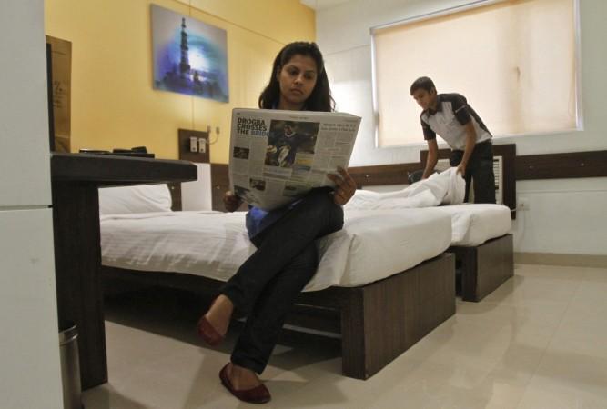 A guest reads a newspaper inside her room as an attendant cleans the bed inside the Tata Group's Indian Hotels Co. Ginger chain in New Delhi May 23, 2012. gst, gst on hotels, gst on restaurants, gst council