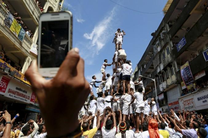 PILING THEM HIGH: A devotee uses a mobile phone to photograph devotees forming a human pyramid to break a clay pot containing curd during celebrations to mark Janmashtami in Mumbai. REUTERS/Danish Siddiqui Telecom
