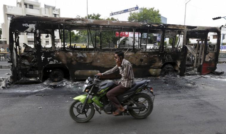 A man rides a motorcycle past the wreckage of a bus that was burnt in the clashes between the police and protesters in Ahmedabad, India, August 26, 2015 Two-wheeler rider in India