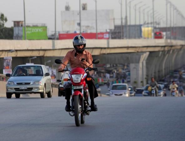 A commuter uses his mobile phone while riding on a motorbike in Rawalpindi, Pakistan June 12, 2017 bike commuter using mobile phone while riding