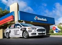 A Ford self-driving delivery vehicle is pictured in front of a Domino's pizza restaurant