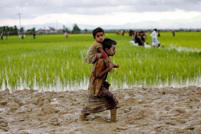 A Rohingya boy carries a child while walking in the mud after crossing the Bangladesh-Myanmar border in Teknaf, Bangladesh (File Photo) A Rohingya boy carries a child while walking in the mud after crossing the Bangladesh-Myanmar border in Teknaf, Bangladesh